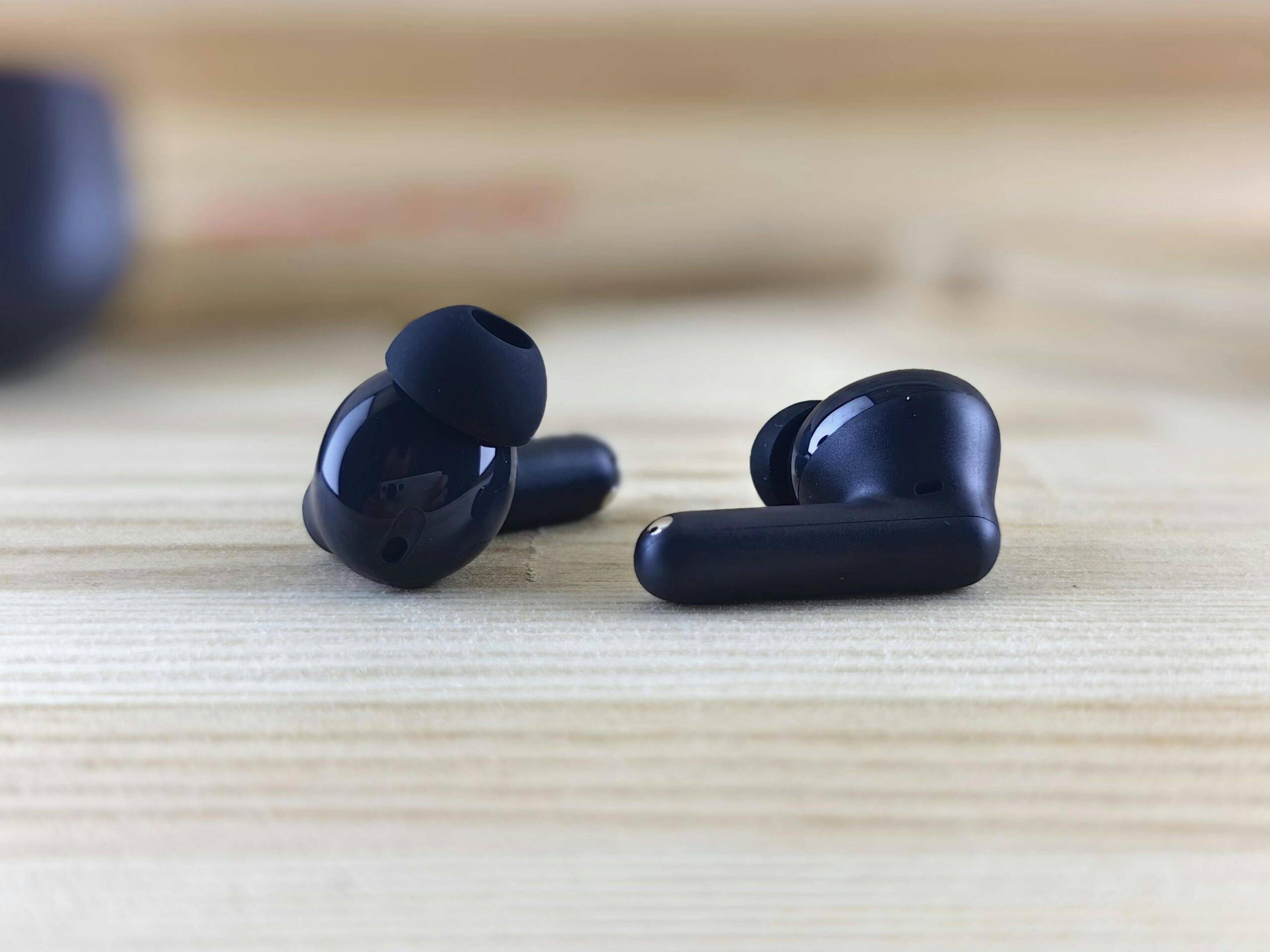 Detailed close-up of sleek wireless earbuds on a natural wooden surface, showcasing modern technology.