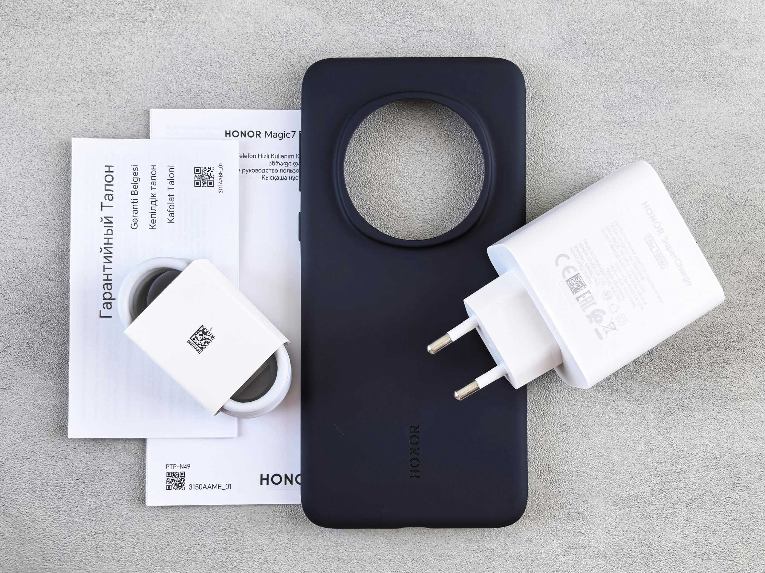 Flat lay of HONOR phone case, charger, and warranty documents on a table.