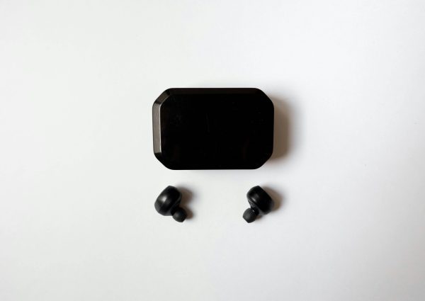 Top view of wireless earbuds with charging case on a white surface, showcasing sleek design and technology.